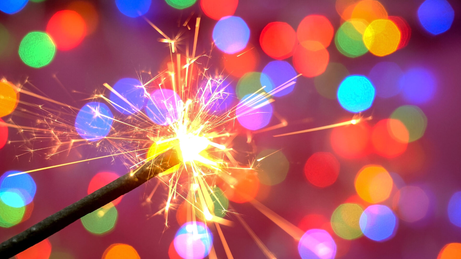 Bright burning sparkler against the backdrop of defocused multic